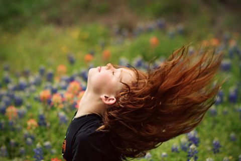 Girl with Red Hair Flipping Her Hair over Head With Her Eyes Closed in a Field of Flowers